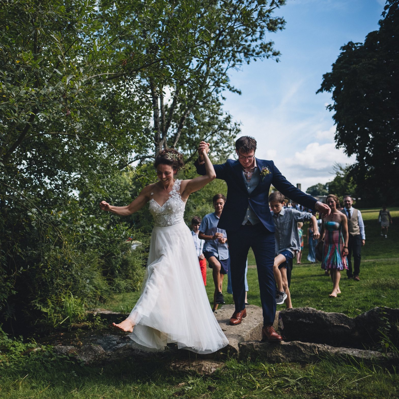 Newlyweds jumping over a stream on their wedding day at Colehayes Park Dartmoor