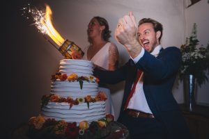 Groom celebrating the massive sparkler firing out of the wedding cake at The Corn Barn Cullompton